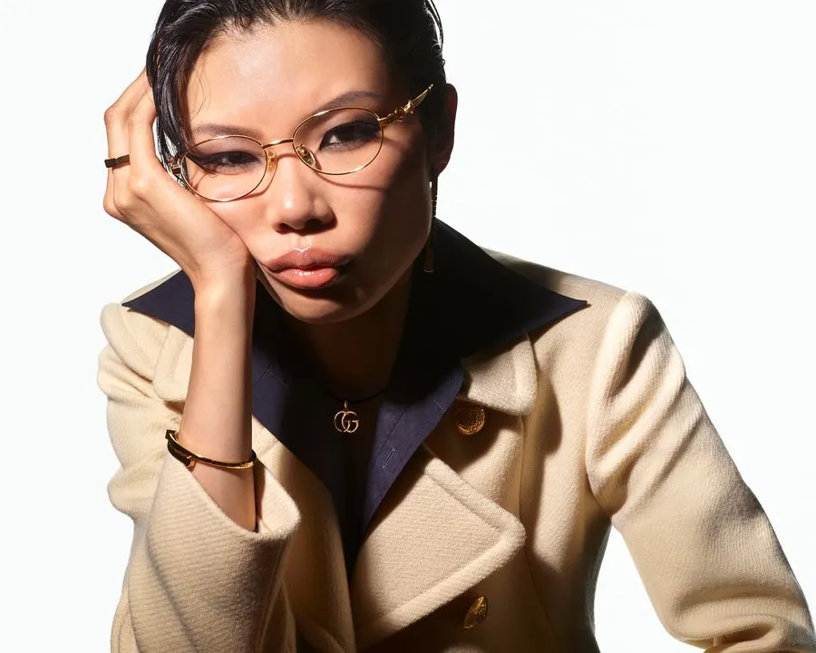 A woman wearing fine gold-rimmed spectacles and a camel coat