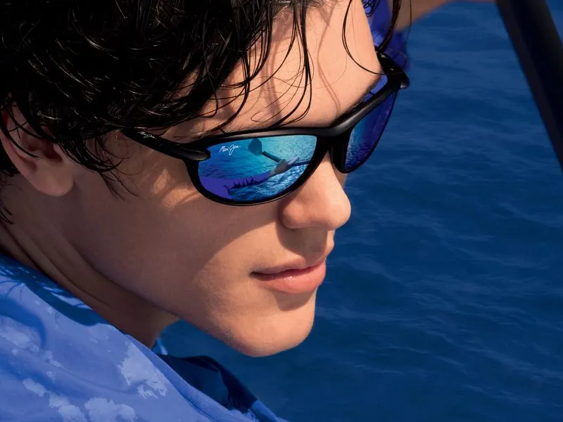 A man in blue mirrored Maui Jim sunglasses beside water