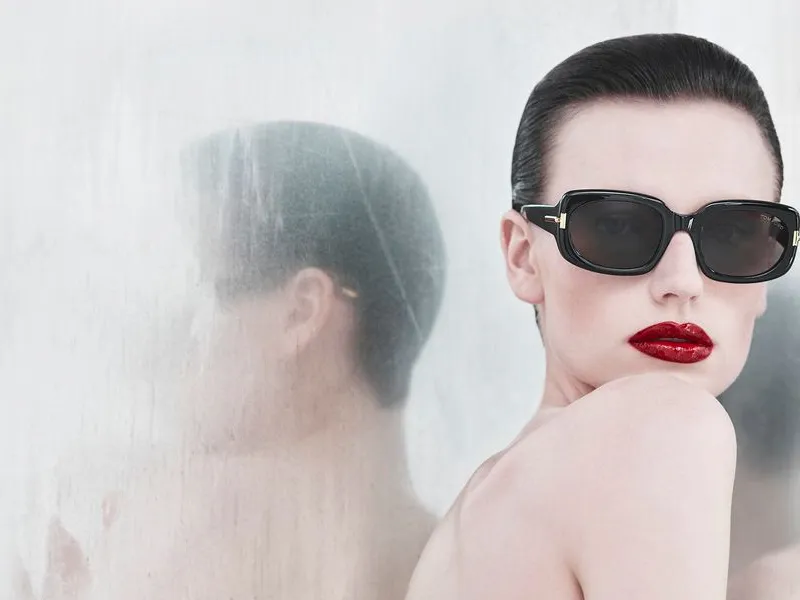 A woman in black Tom Ford sunglasses against a pale studio backdrop