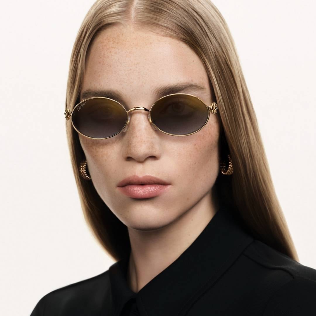 A woman wearing slim oval Clash de Cartier sunglasses with decorated temples