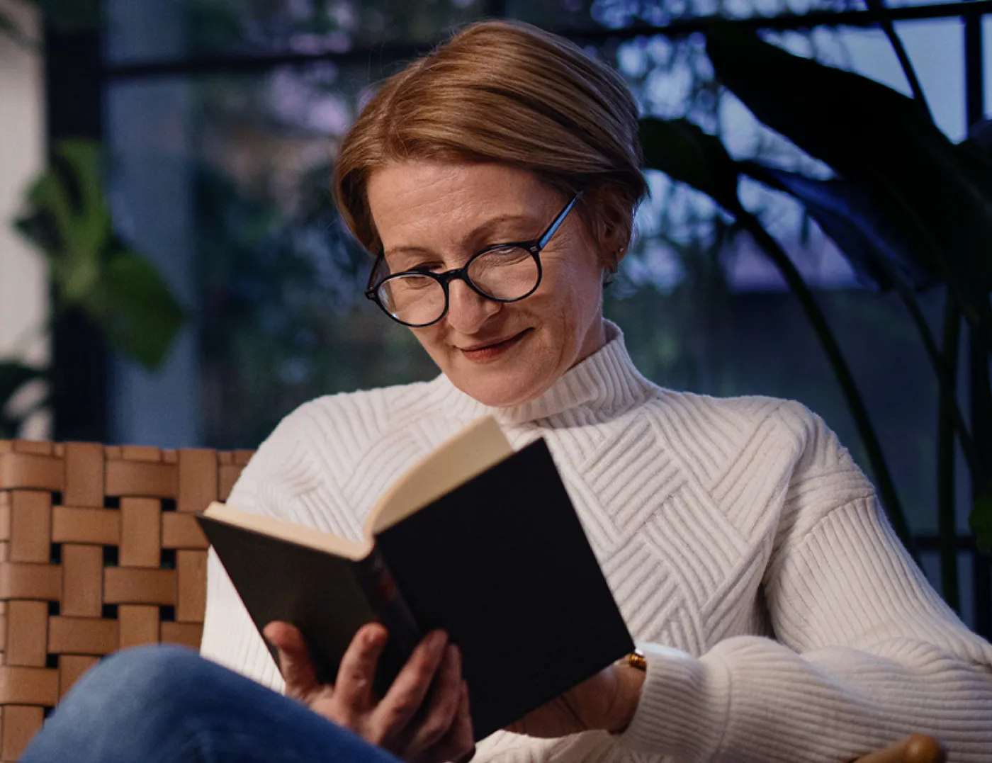 A woman reading a book through spectacles in low, warm light